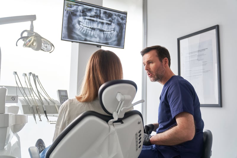 Dentist discussing X-ray results with a patient in a modern dental office, highlighting the importance of secure, fast payment solutions for dental practices—powered by Virtue Payments.