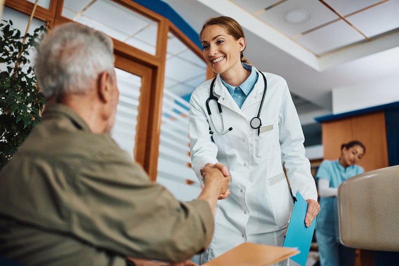 Specialist warmly greeting an older patient in a medical office, representing the personalized care and flexible payment solutions Virtue Payments offers to specialty healthcare providers.
