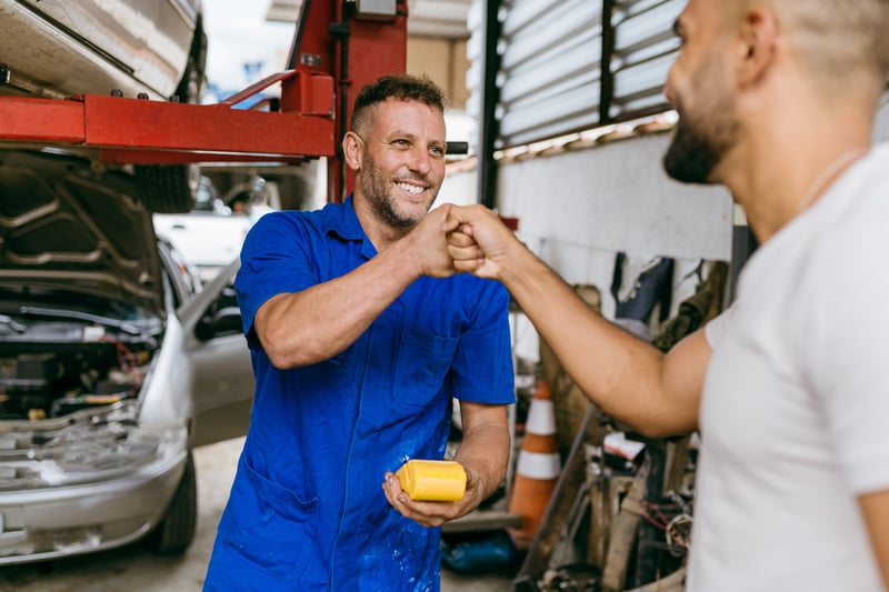 Car repair shop owner accepting payment from happy customer on mobile wireless credit card terminal he can carry around