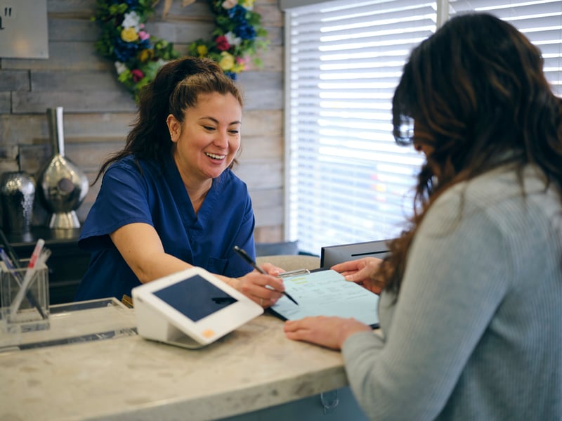Healthcare receptionist assisting patient at front desk with Clover mini used for patient payments in a modern medical or dental practice