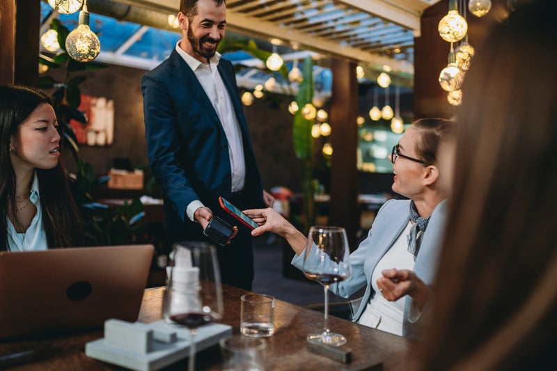 Employee accepting table-side contactless credit card payment at high end fine dining hotel restaurant resulting in a happy customer