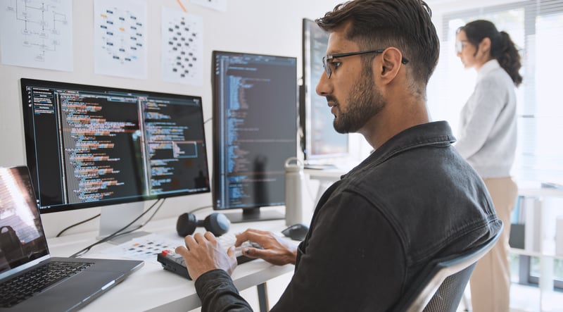 Focused developer writing code at multi-monitor workstation in modern office, illustrating backend software integration for fintech platforms